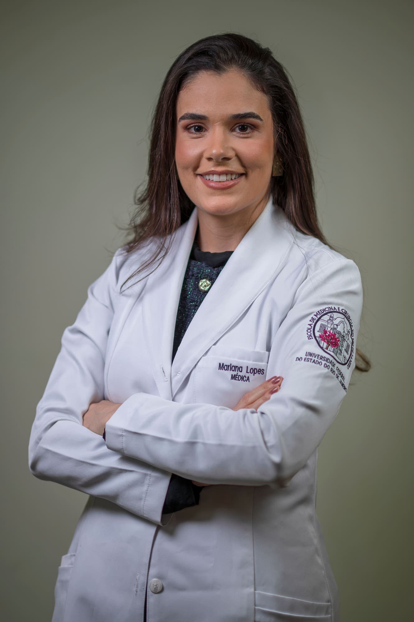 Dra. Mariana Lopes de jaleco, de braços cruzados, sorrindo